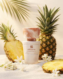 Flacon blanc Olfazeta by Chogan Millésime N°85 entouré d'ananas et de fleurs blanches sur sable ensoleillé